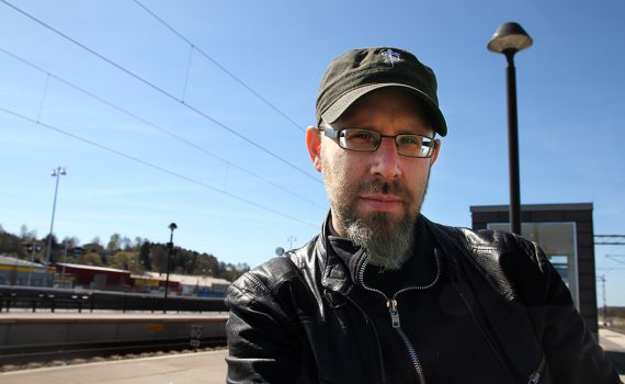 Professor Klas Rönnbäck på tågstation mot blå himmel.