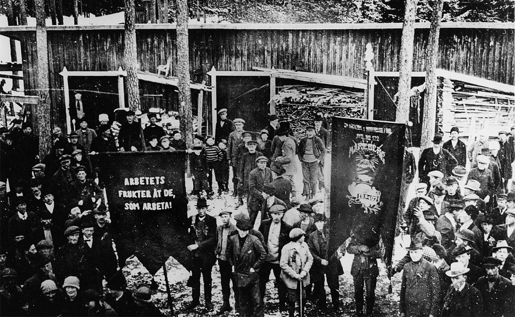 Svartvit bild på fackföreningsmedlemmar 1917 vid Mariebergs sågverk i Ådalen, ”Arbetets frukter åt de, som arbeta!”