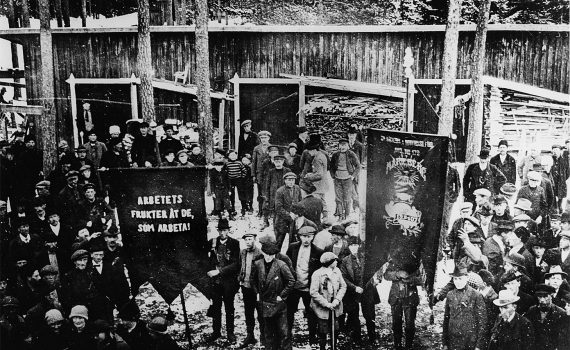 Svartvit bild på fackföreningsmedlemmar 1917 vid Mariebergs sågverk i Ådalen, ”Arbetets frukter åt de, som arbeta!”