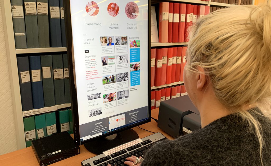 En sittande kvinna med uppsatt hår tittar på en bildskärm, där ARABs webbplats syns. I en vit bokhylla bakom skärmen står blå och röda kontorspärmar.
